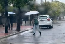 Córdoba: el SMN emitió alertas amarilla y naranja por tormentas y granizo Calle urbana bajo una lluvia intensa, con personas usando paraguas, pavimento mojado y agua acumulada